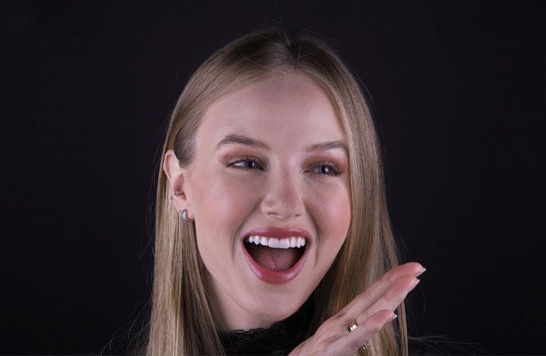 Imagem do rosto da Kelin direcionado para a direita, com aparência de surpresa, mostrando os dentes em que foi feita a cosmética com resina composta.